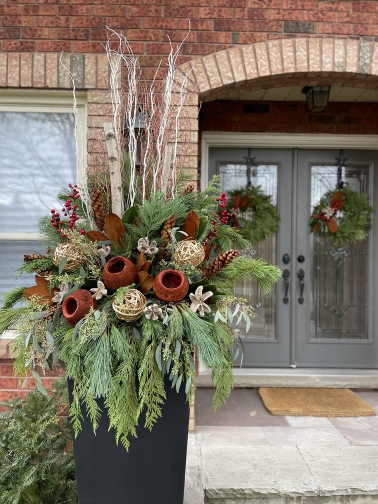 Winter planter in burgundy and copper with magnolia leaves, birch and evergreen at a brick entry