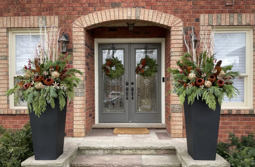 Arched brick entry with matching evergreen wreaths and two tall winter planters of cedar, birch and red accents