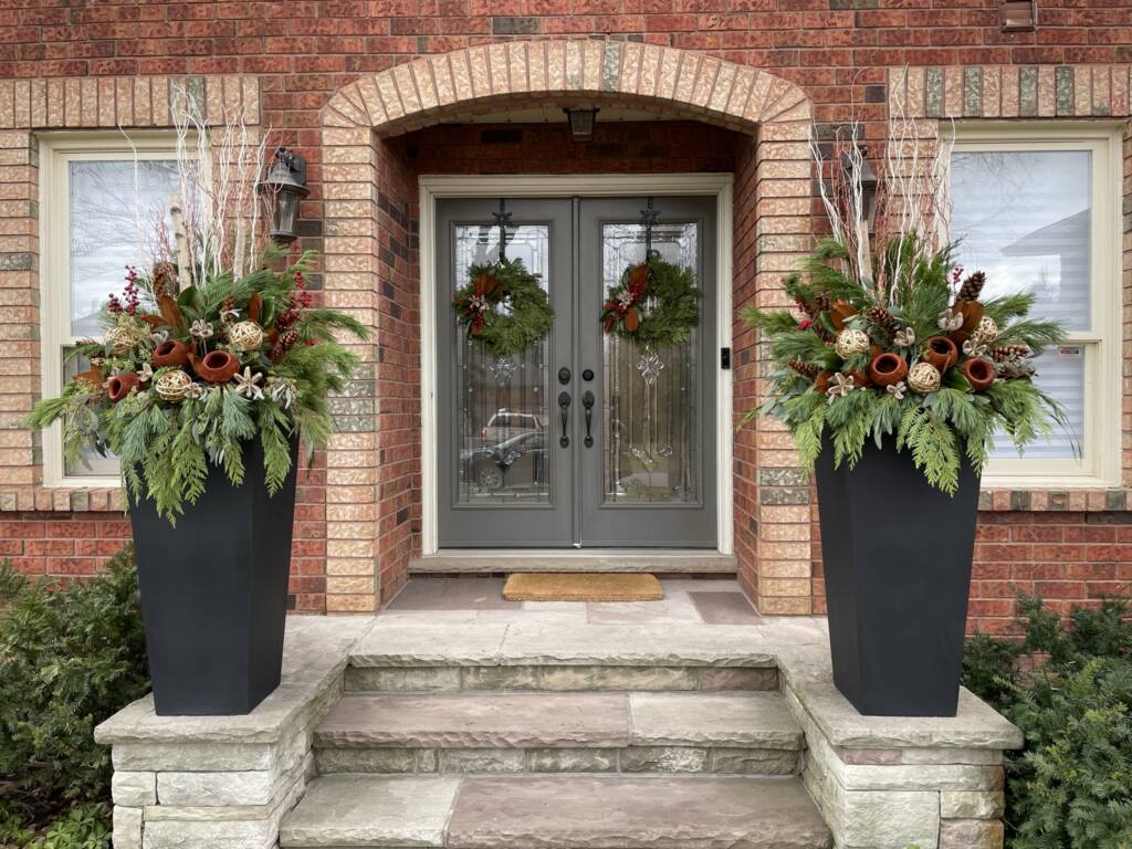 Brick entry with evergreen wreaths and matching red winter planters