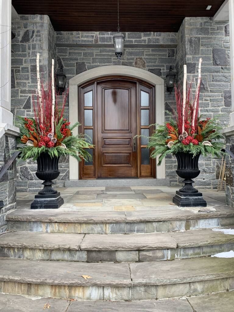 Classical black urns with tall red spikes flanking a wooden front door