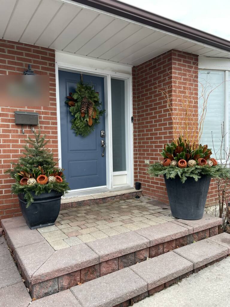 Pair of grey planters with magnolia and orange pods at a blue front door