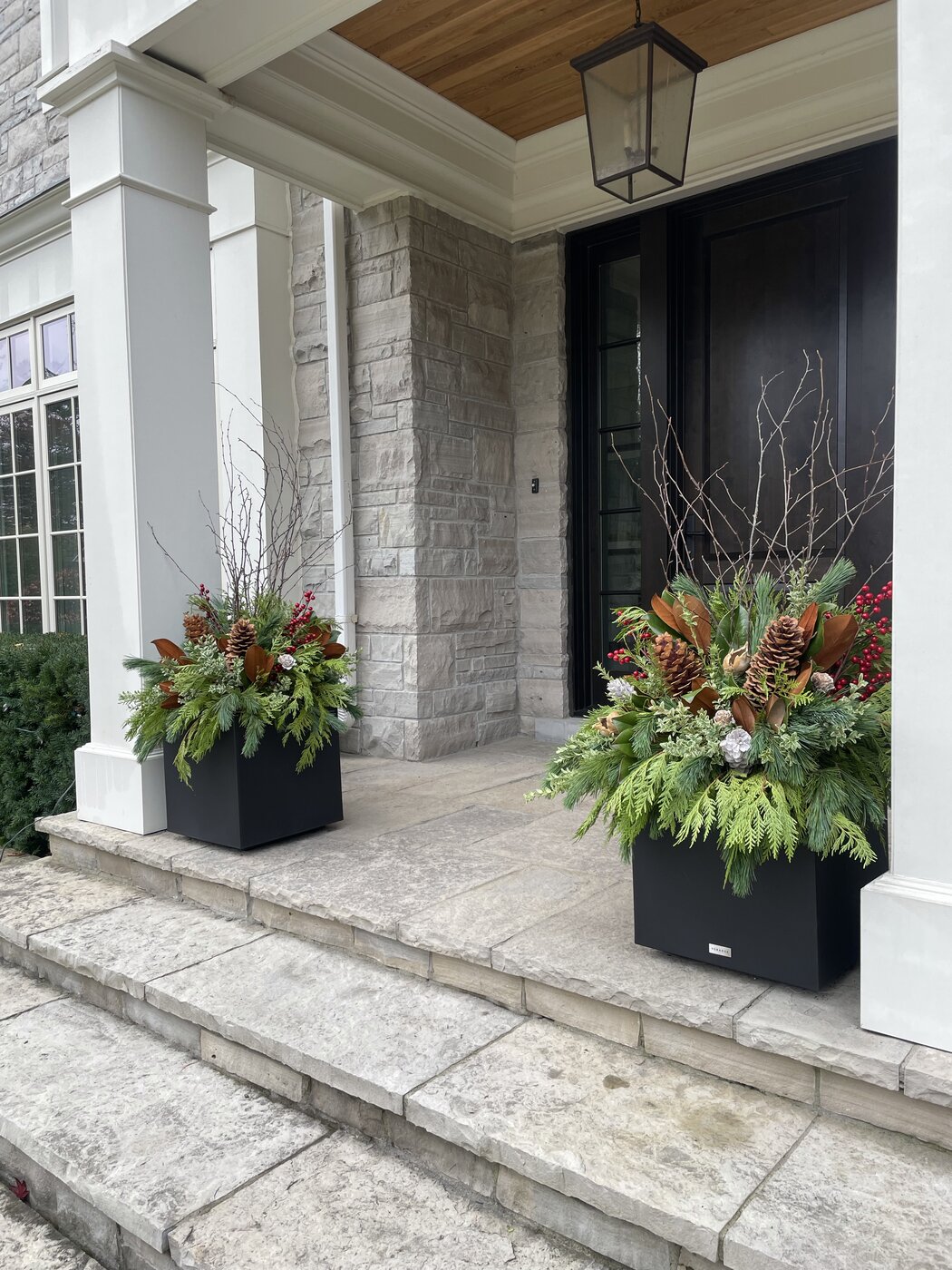 Two black planters with evergreen arrangements flanking a dark front door with white columns