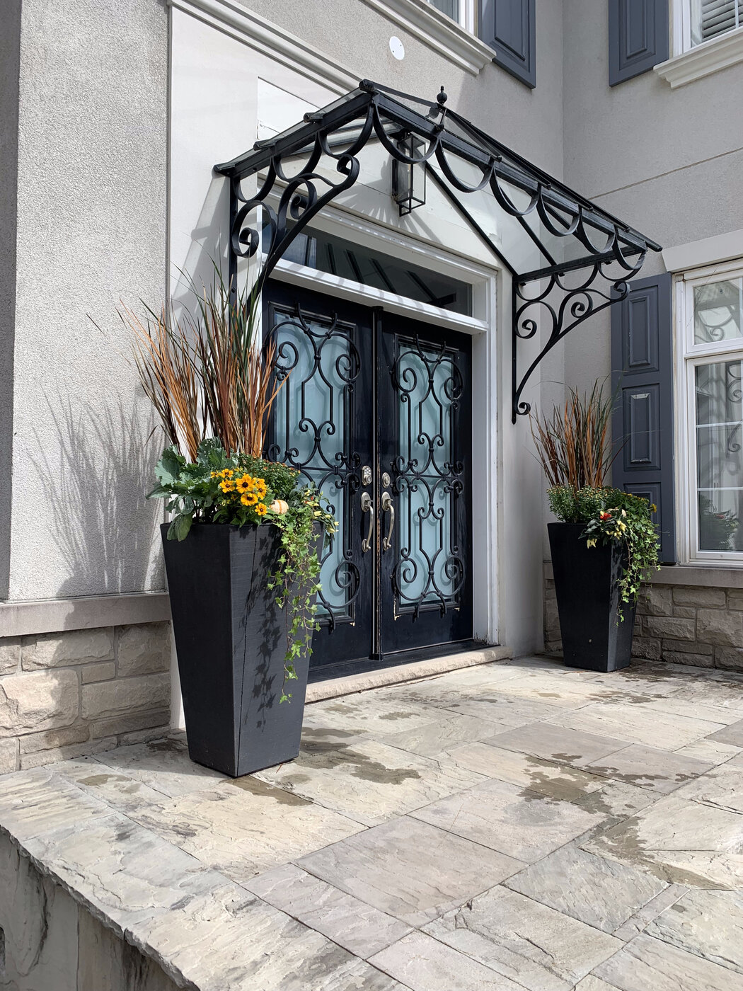 A matched pair of tall black tapered planters flanking an iron and glass double door